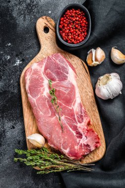 Çiğ domuz pirzolası. Bir parça çiğ et, yeşillik ve baharatla hazırlanmaya hazır. Siyah arka plan. Üst görünüm