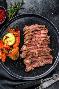 Dilimlenmiş sığır eti, az pişmiş biftek. Yanında sebze tabağı olan bir tabakta yuvarlan. Siyah arka plan. Üst görünüm