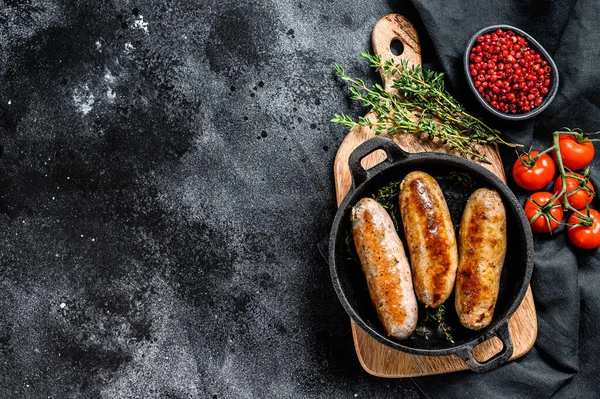 Tasty homemade sausages in a skillet. Pork, beef and chicken meat. Black background. Top view. Copy space.