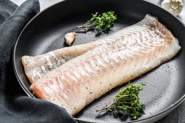 Çiğ morina filetosu ve tavada otlar. Gri arka plan. Üst görünüm.