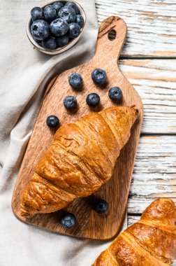 Taze kruvasan ve yabanmersinli lezzetli bir kahvaltı. Beyaz ahşap arka plan. Üst görünüm.