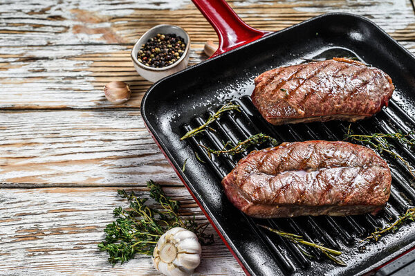 Grilled meat Top Blade steaks in a frying pan. Gray background. Top view. Copy space.