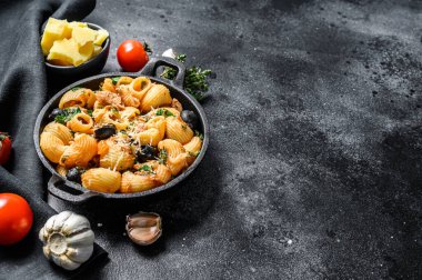 Geleneksel İtalyan makarnası domates, zeytin, kapari, ançüez. Conchiglie rigate, puttanesca. Siyah arka plan. Üst Manzara. Boşluğu kopyala.