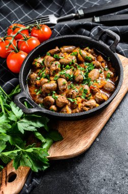 Fırında pişirilmiş tavuk ciğeri kalpleri dökme demir tavada. Siyah arka plan. Üst görünüm.