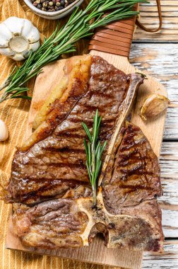Kesme tahtasında ızgara biftek. Pişmiş tbone biftek. Beyaz ahşap arka plan. Üst görünüm.