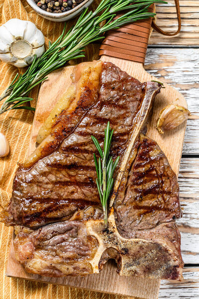 Жареный стейк из кости на доске для рубки. Сваренная говядина. Белый деревянный фон. Вид сверху.