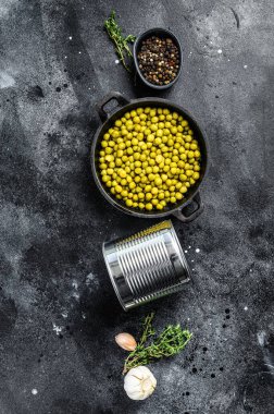 Dökme demir kasede yeşil bezelyeler. Konserve yiyecekler. Siyah arka plan. Üst görünüm.