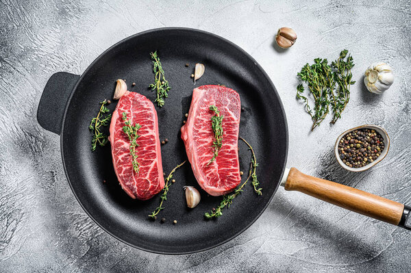 Raw top-blade steak in a pan. Gray background. Top view.