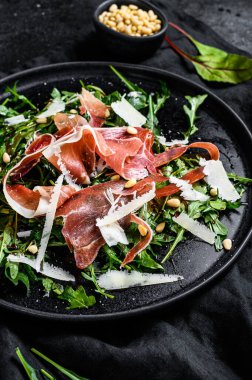 Serrano jamon, jambon, roka ve parmesan peynirli salata. Siyah arkaplan, üst görünüm