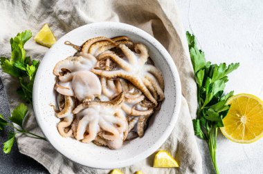 Beyaz kasede maydanozlu çiğ ahtapot ve limon. Organik deniz ürünleri. Gri arka plan. Üst görünüm.