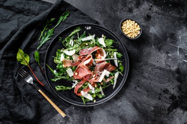 Serrano jamon, jambon, roka ve parmesan peynirli salata. Siyah arkaplan, üst görünüm