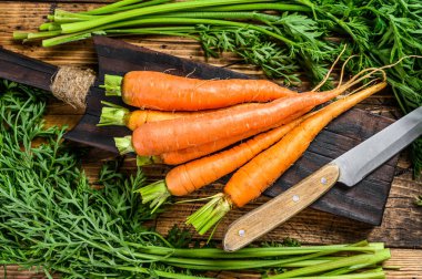 Kesme tahtasında yaprakları olan turuncu havuçlar. Ahşap arka plan. Üst görünüm