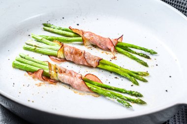 Pişirme kabında kuşkonmaz etrafında lezzetli domuz pastırması. Siyah arka plan. Üst görünüm.