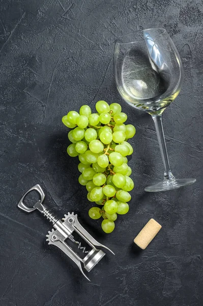 A branch of green grapes, a wine glass, a corkscrew and a cork. Concept of wine-making. Black background. Top view.