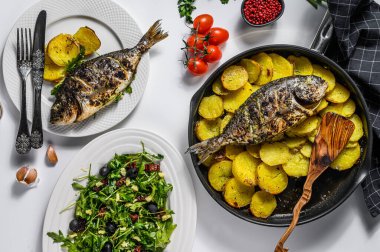 Izgara balık, domatesli roka salatası, fırında patates. Beyaz arka plan. en üstteki görünüm.