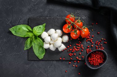 Mini mozzarella peyniri, fesleğen yaprağı ve vişneli domates, Caprese salatası. Siyah arka plan. en üstteki görünüm.