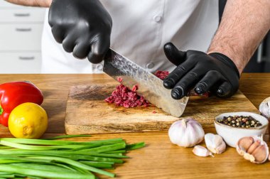 Adam çiğ et kesiyor. Siyah eldivenli bir şef. Etli tartar pişirme kavramı.