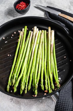 Kızartma tavasında yeşil kuşkonmaz pişirmek. Siyah arka plan. Üst görünüm.