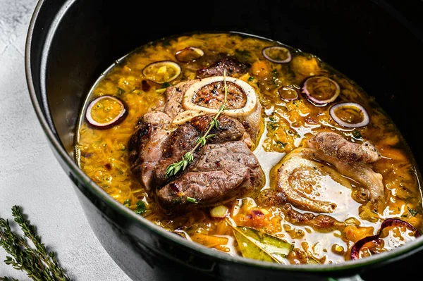 Çapraz kesilmiş dana bacağından yapılmış ossobuco ile demir tava. Ossobuco et yahnisi. Gri arka plan. Üst görünüm.