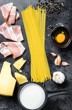Geleneksel İtalyan alla carbonara makarna malzemeleri. Pişmemiş spagetti, pancetta pastırması, parmesan peyniri, yumurta. Siyah arka plan. Üst görünüm.
