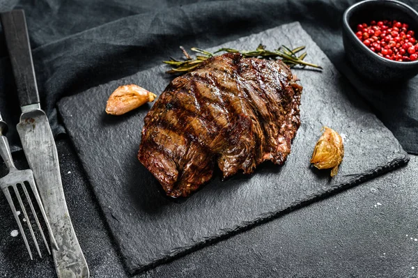 Grilled Flat Iron steak on a stone Board, marbled beef. Black background. Top view.