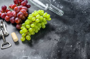 Bir dal yeşil ve kırmızı üzüm, boş bir şişe, bir tirbuşon ve bir mantar. Ev yapımı şarap kavramı. Siyah arka plan. Üst Manzara. Boşluğu kopyala.