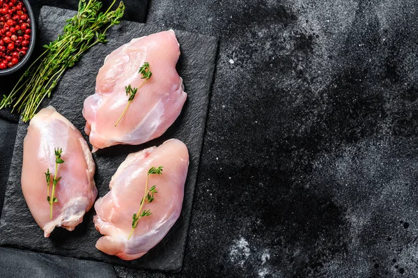 Chicken thigh fillet without skin. Black background. Top view. Copy space.