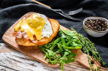 Pastırmalı kahvaltı burgeri, Benedict yumurtası, brioche ekmeğine Hollandaise sosu. Arugula salatalı garnitür. Beyaz arka plan. Üst görünüm.