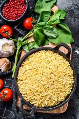 Bir kase pişmemiş, fesleğenli, domatesli ve sarımsaklı Orzo makarna. Siyah arka plan. Üst görünüm