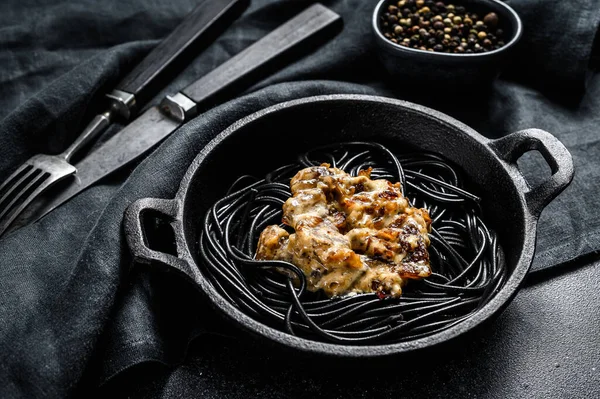 Tavada mürekkep balığı mürekkebi olan siyah spagetti makarna. Biber soslu biftek. Siyah arka plan. Üst görünüm.