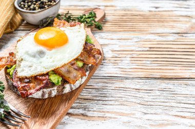 İngiliz kahvaltısı, pastırmalı tost, avokado ve kesilmiş yumurta. Sağlıklı yiyecekler. Beyaz ahşap arka plan. Üst Manzara. Boşluğu kopyala.