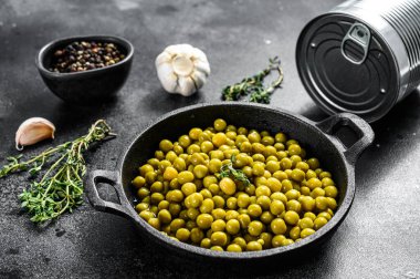 Kızartma tavasında konserve yeşil bezelye. Konserve yiyecekler. Siyah arka plan. Üst görünüm.