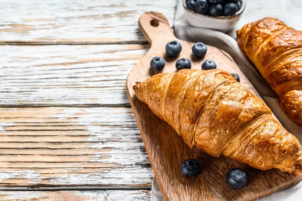Taze kruvasan ve yabanmersinli lezzetli bir kahvaltı. Beyaz ahşap arka plan. Üst Manzara. Boşluğu kopyala.