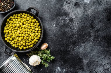 Dökme demir kasede yeşil bezelyeler. Konserve yiyecekler. Siyah arka plan. Üst Manzara. Boşluğu kopyala.