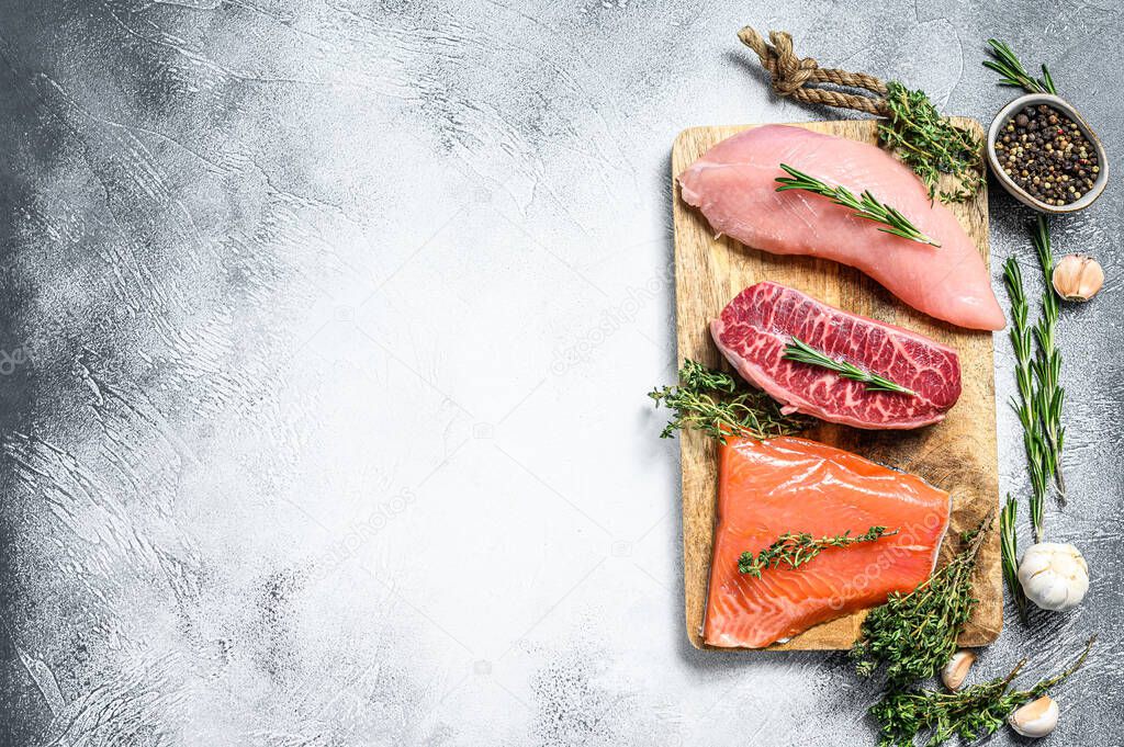 Different types of raw meat on cutting board with herbs. Beef top blade, salmon fillet and Turkey breast. steaks. White background. Top view. Copy space.