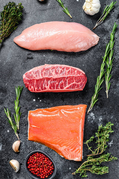 Raw steaks. Beef top blade, salmon fillet and Turkey breast. Organic fish, poultry and beef meat. Black background. Top view.