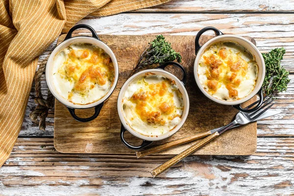 Julienne, ahşap bir masada porsiyon şeklinde tavuk ve peynirle. Beyaz arka plan. Üst görünüm.