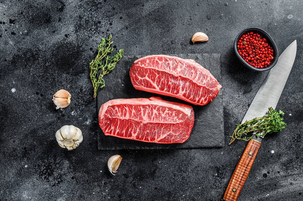 Raw top blade steak dry-aged on a stone board. Black background. Top view