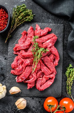 Stroganoff bifteği için ince dilimler halinde kesilmiş çiğ et. Siyah arka plan. Üst görünüm.