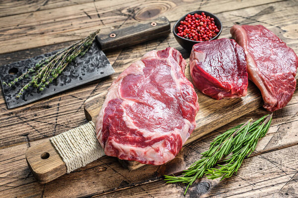 Variety of raw black angus beef meat steaks fillet Mignon, rib eye or cowboy, Striploin or new york. Wooden background. Top view.