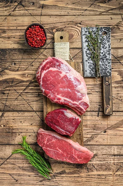 Variety of raw black angus beef meat steaks fillet Mignon, rib eye or cowboy, Striploin or new york. Wooden background. Top view.