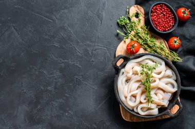 Çiğ mürekkep balığı kızartma tavasında halka şeklinde kesilmiş. Siyah arka plan. Üst Manzara. Boşluğu kopyala.