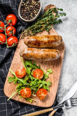 Izgara domuz sosisi, yanında da domates salatası ve roka. Gri arka plan. Üst görünüm.