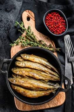 Metal tavada servis edilen tam yağda kızartılmış kapelinli balık. Siyah arka plan. Üst görünüm.