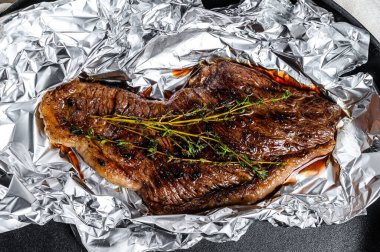 Grilled sirloin steak in foil. Black background. Top view. clipart