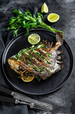 Limonlu kızarmış Dory balığı ve tavada maydanoz. Vejetaryen sağlıklı yiyecekler. Siyah arka plan. Üst görünüm.