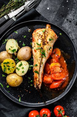 Domateslerin içinde patates ve sebzelerle pişirilmiş maymunbalığı. Siyah arka plan. Üst görünüm.