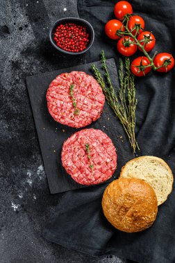 Hamburger pişirmek için gerekli malzemeler. Kıymalı börek, çörek, domates, otlar ve baharatlar. Siyah arka plan. Üst görünüm.
