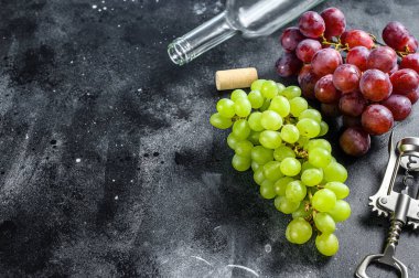 Bir dal yeşil ve kırmızı üzüm, bir şişe, bir tirbuşon ve bir mantar. Şarap yapma kavramı. Siyah arka plan. Üst Manzara. Boşluğu kopyala.