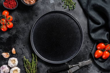 Taze çiğ sebze ve sebzelerin ortasında siyah tabak. Sağlıklı, temiz yemek, vejetaryen, diyet yemek konsepti. Siyah arka plan. Üst Manzara. Boşluğu kopyala.